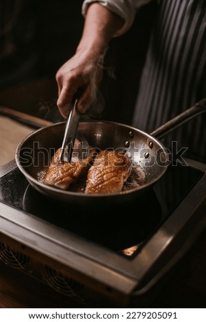 The process of cooking a duck breast, frying and baking in a pan, chef, male cook's hands, in dark tones, juicy close-up, fat fried butter, raw meat