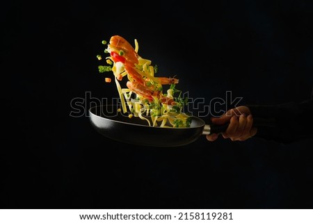 The process of cooking Italian pasta with seafood and vegetables by a professional chef in a restaurant. Food on a black background in a frozen flight. The concept is cooking dishes with seafood.