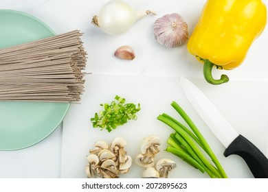 The Process Of Cooking Soba - Buckwheat Japanese Noodles. On A Cutting Board, Chopped Green Onions, Uncooked Soba, Garlic, White Onions, Yellow Bell Pepper. Selective Focus Planned