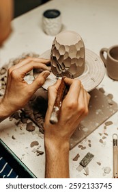 The process of creating a ceramic mug by hand. The master carefully designs the texture of the product on the potter's wheel. Atmospheric photo shows the art of pottery and manual work with clay.