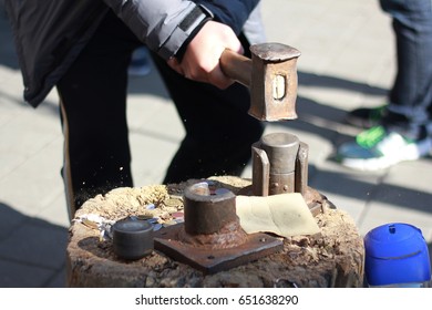 The process of creating a coin manually. Man hitting the press with a hammer to create a coin.