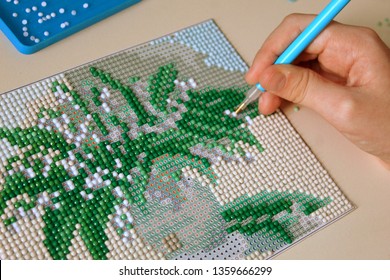 The process of creating a diamond mosaic of a picture of a vase with spring branches, selective focus.