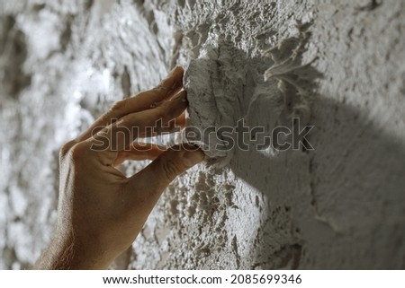 Process of creating white textured clay wall with cracks and imperfections using sstones. Wall design ideas in contemporary interior. 
