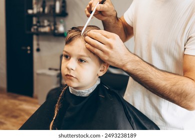 process of cutting a blond boy with a long braid in a chair in a barbershop salon, a barbershop concept for men and boys - Powered by Shutterstock