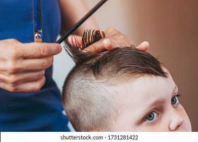 The process of cutting a child's hair. Close-up of women's hands making a stylish haircut for a little boy