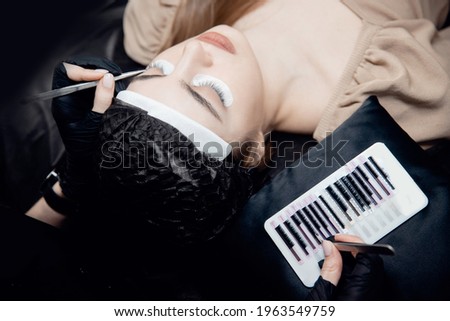 Process Eyelash extension procedure top view. Master tweezers fake 2d lashes beautiful female eyes.