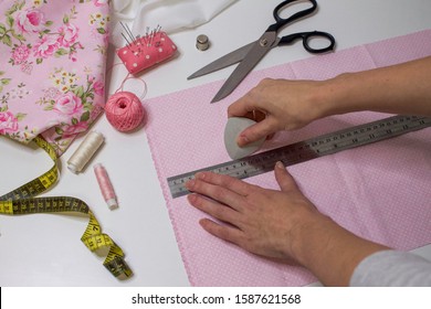 The process of hand sewing with fabric, scissors, accessories for sewing. Hands in chalk draw a line with a ruler on cotton.