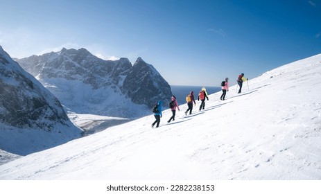 Process of hiking in Northern Norway, Lofoten Islands, Nordland, on the way to Ryten mountain and Kvalvika beach, with a groups of hikers, and mountains around, sunny winter day