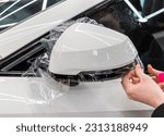 The process of installing PPF on the side of the car. PPF is a polyurethane, protective film that protects the paint from scratches and gravel. Armored film on the car mirror. Car wrapping close-up.