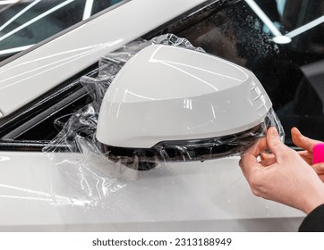 The process of installing PPF on the side of the car. PPF is a polyurethane, protective film that protects the paint from scratches and gravel. Armored film on the car mirror. Car wrapping close-up.