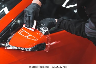 The process of installing PPF on the side mirror of a red sports car. Protective film for paint protecting scratches and gravel. High quality photo