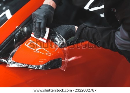 The process of installing PPF on the side mirror of a red sports car. Protective film for paint protecting scratches and gravel. High quality photo