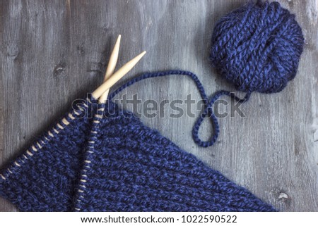 Process of knitting. Ball of blue woolen thread and knitting needle closeup on wooden table in rustic. Needlecraft backgtound. Crochet backdrop