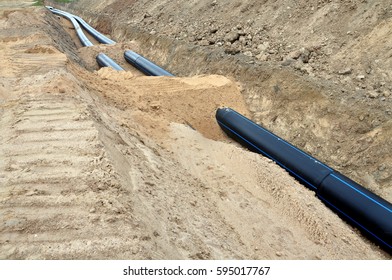 The process of laying of engineering and heating systems. Black plastic pipes are in a trench of sand in perspective.