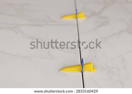 The process of laying light ceramic tiles or porcelain tiles with a marble effect using a tile leveling system. Plastic clamp and wedge at the joint of porcelain tiles with a marble pattern. Repair