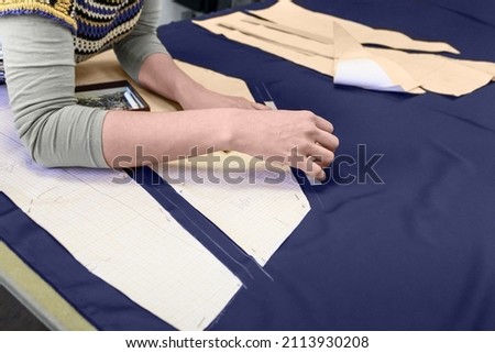 The process of laying out the details of the pattern on the fabric. Women's hands that outline seam allowances with tailor's chalk. Concept: atelier, sewing and sewing courses, sewing hobby.
