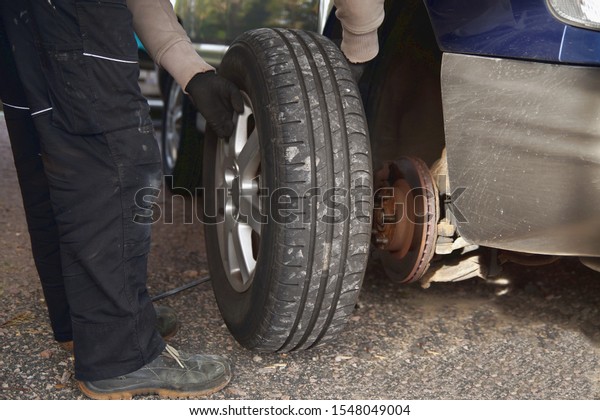 Process of maintenance. man holding a tire at the\
garage. Replacement of winter and summer tires. Seasonal Tires\
Replacement concept. 