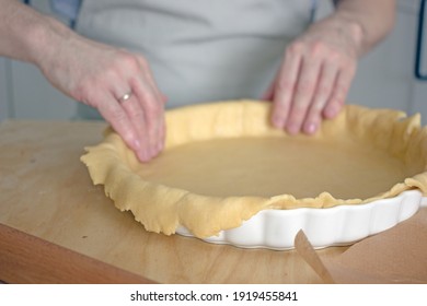 The process of making a base for a shortcrust quiche pie, male hands transfer a rolled dough sheet into a baking dish. Authentic home hobby home baker. Pie crust recipe