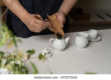 The Process Of Making Chinese Tea. Someone Puts Tea Leaves In A Ceramic Teapot. Blurred Background