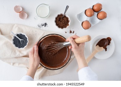 The Process Of Making A Chocolate Cake. Female Hands Stir The Chocolate Dough. Poppy Seed Cake On A White Plate.