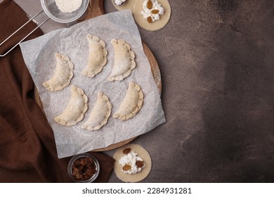 Process of making dumplings (varenyky) with cottage cheese. Raw dough and ingredients on brown table, flat lay. Space for text