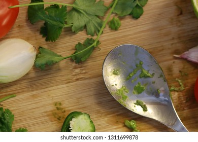 Process Of Making Guacamole - Mexican Avocado Salsa. In This Photo You Can See Some Of Guacamole Ingredients On A Cutting Board. There Are Tomato, Chili, Garlic, Onion, Cilantro, Spoon. Macro Photo.