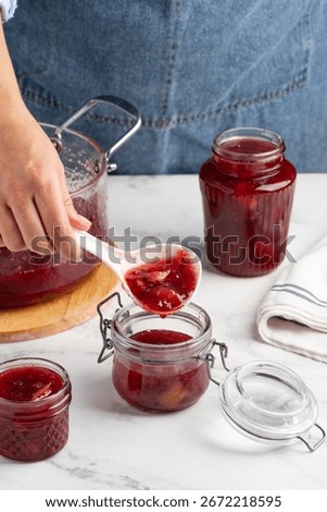 The process of making lingonberry pear jam. A woman pours jam into jars.