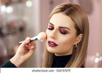 Process of making makeup. Make-up artist working with brush on model face. Portrait of young blonde woman in beauty saloon interior. Applying tone to skin.