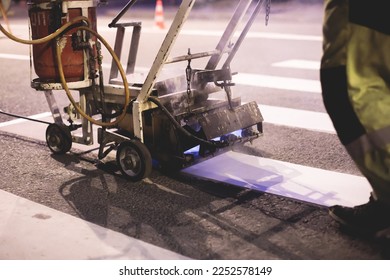 Process of making new road surface markings with a line striping machine, workers improve city infrastructure, demarcation marking of pedestrian crossing with hot melted paint on asphalt pavement