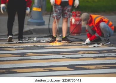 Process of making new road surface markings with a line striping machine, workers improve city infrastructure, demarcation marking of pedestrian crossing with a hot melted paint on asphalt pavement