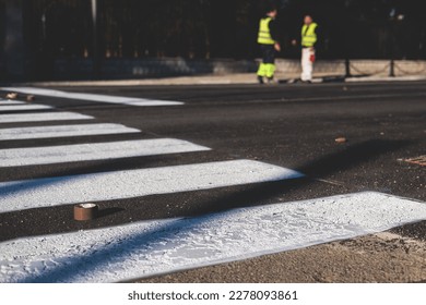 Process of making new road surface markings with a line striping machine, workers improve city infrastructure, demarcation marking of pedestrian crossing with hot melted paint on asphalt pavement
