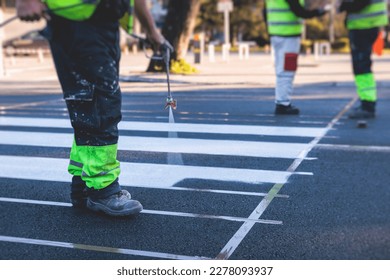 Process of making new road surface markings with a line striping machine, workers improve city infrastructure, demarcation marking of pedestrian crossing with hot melted paint on asphalt pavement
