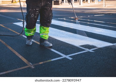Process of making new road surface markings with a line striping machine, workers improve city infrastructure, demarcation marking of pedestrian crossing with hot melted paint on asphalt pavement
				
