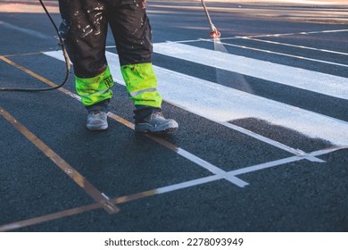 Process of making new road surface markings with a line striping machine, workers improve city infrastructure, demarcation marking of pedestrian crossing with hot melted paint on asphalt pavement
