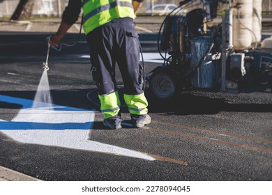 Process of making new road surface markings with a line striping machine, workers improve city infrastructure, demarcation marking of pedestrian crossing with hot melted paint on asphalt pavement

