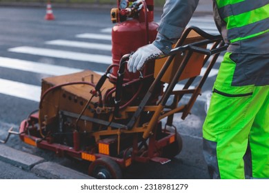 Process of making new road surface markings with a line striping machine, workers improve city infrastructure, demarcation marking of pedestrian crossing with hot melted paint on asphalt pavement
