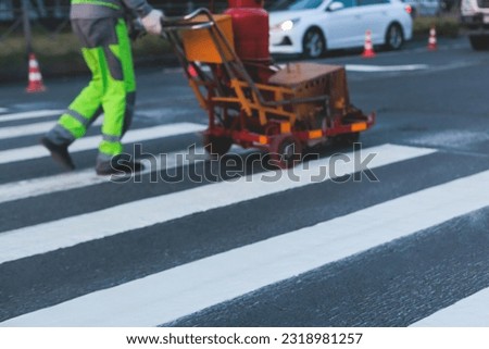 Process of making new road surface markings with a line striping machine, workers improve city infrastructure, demarcation marking of pedestrian crossing with hot melted paint on asphalt pavement
