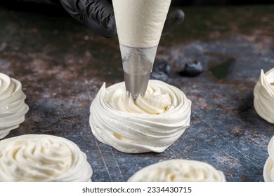 The process of making Pavlova dessert. The confectioner fills the dessert with cream using a pastry bag