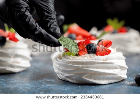 The process of making Pavlova dessert. Decorating the Pavlova dessert with fresh slices of strawberries, blueberries and mint leaves