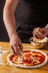 The Process Of Making Pizza. Pizzaiolo Tops The Dough With Grated Mozzarella Cheese. Vertical. Dark Background.