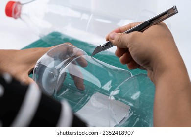 The process of making plant pots from plastic bottles. Hand cutting a plastic bottle with a cutter to grow plants or vegetables inside. Recycle and reusable green garden concept.