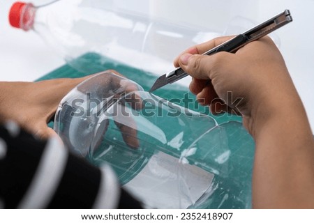 The process of making plant pots from plastic bottles. Hand cutting a plastic bottle with a cutter to grow plants or vegetables inside. Recycle and reusable green garden concept.