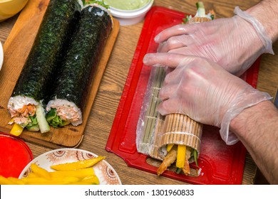 Process of making sushi and rolls. Close-up of man chef hands preparing traditional Japanese food at home or in restaurant on kitchen table.