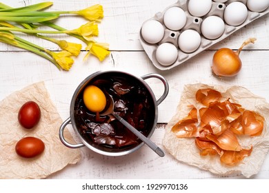 the process of painting Easter eggs with natural vegetable dyes, onion husks, on a white wooden background, a top view of chicken eggs and yellow daffodils.