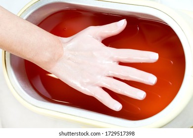 The process of paraffin therapy of a female hand is shot close up in a beauty salon.

