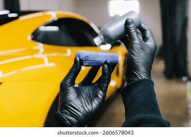 Process of pouring ceramic liquid from bottle on sponge to apply a protective nano layer on car. Detailing service worker applies ceramic protective liquid on sponge close-up