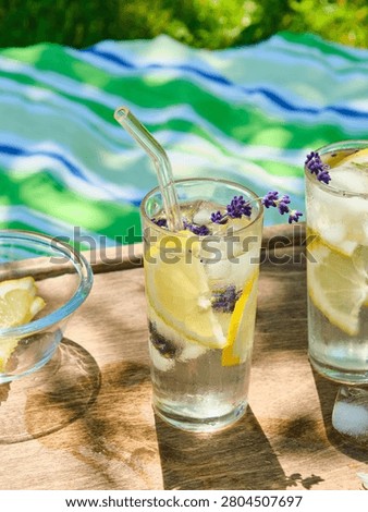 The process of preparing cold water with lemon and ice cubes in tall glasses outdoors in summer. Refreshing drinks.
