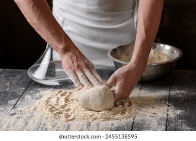 The process of preparing dough. A cook kneads dough from whole grain wheat flour in the kitchen. Water and flour on a wooden table. Baking baked goods or pizza. Chef's hands close-up. - Powered by Shutterstock