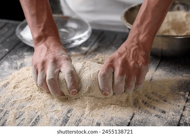 The process of preparing dough. A cook kneads dough from whole grain wheat flour in the kitchen. Water and flour on a wooden table. Baking baked goods or pizza. Chef's hands close-up. - Powered by Shutterstock