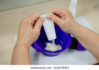 The Process Of Preparing For Hair Coloring At Home. Female Hands Squeeze Hair Dye From A Tube Into A Plastic Bowl. Step 1